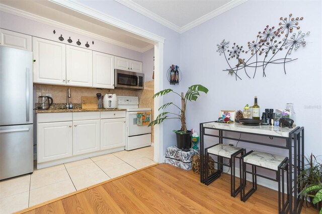 kitchen featuring appliances with stainless steel finishes, light hardwood / wood-style flooring, white cabinets, tasteful backsplash, and crown molding