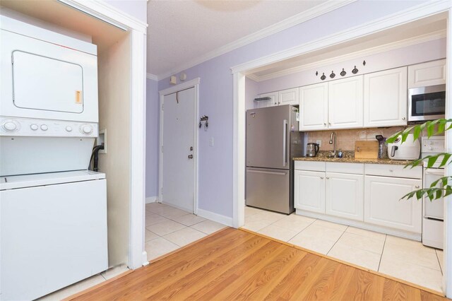 kitchen with appliances with stainless steel finishes, white cabinets, light hardwood / wood-style floors, decorative backsplash, and stacked washer / dryer