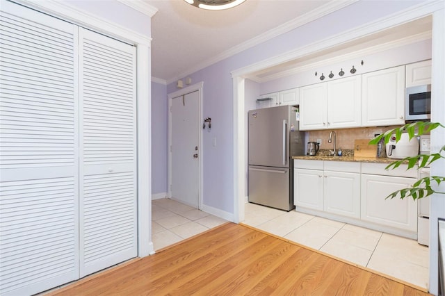 kitchen featuring light hardwood / wood-style flooring, stainless steel appliances, backsplash, crown molding, and white cabinetry