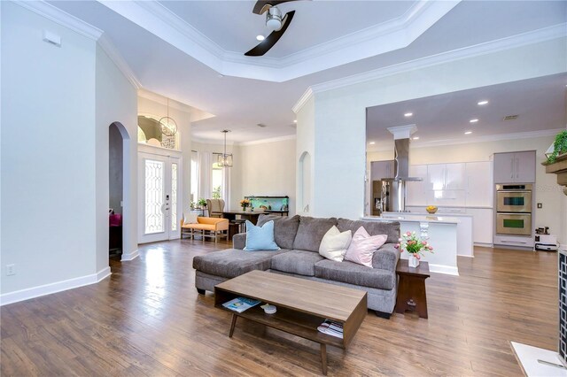 living room with dark wood-type flooring, a raised ceiling, ornamental molding, and a notable chandelier