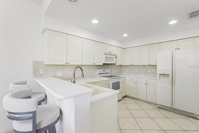 kitchen featuring light tile patterned flooring, white cabinetry, a kitchen breakfast bar, kitchen peninsula, and white appliances