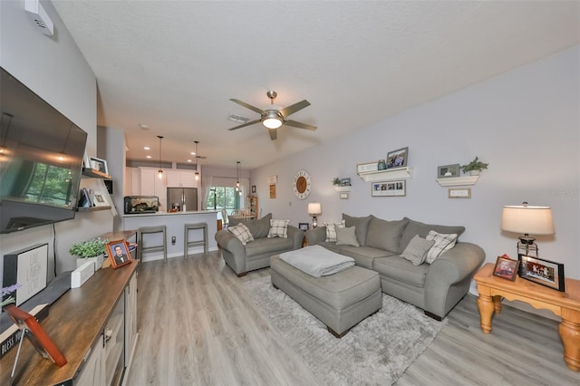 living room featuring ceiling fan, light hardwood / wood-style flooring, and a textured ceiling