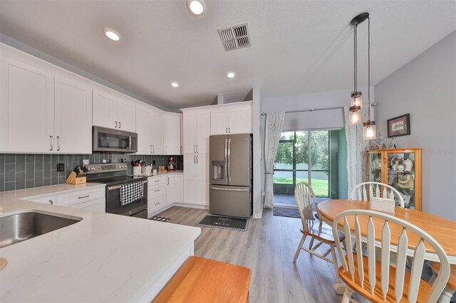 kitchen featuring tasteful backsplash, stainless steel appliances, white cabinets, decorative light fixtures, and light hardwood / wood-style floors