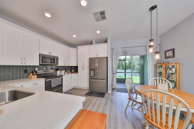 kitchen with pendant lighting, light hardwood / wood-style flooring, appliances with stainless steel finishes, white cabinetry, and tasteful backsplash