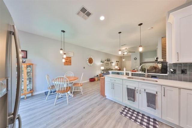 kitchen with white cabinetry, light hardwood / wood-style flooring, backsplash, pendant lighting, and sink