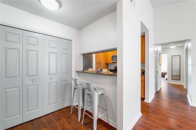 kitchen featuring a kitchen bar, brown cabinets, stainless steel microwave, dark countertops, and dark wood finished floors