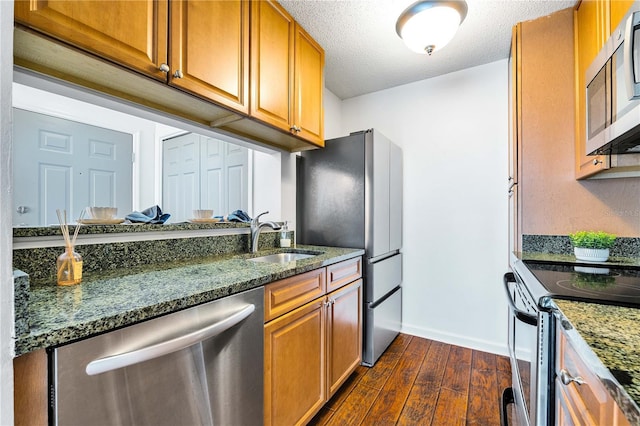 kitchen with dark stone countertops, dark wood-style floors, a sink, appliances with stainless steel finishes, and brown cabinets