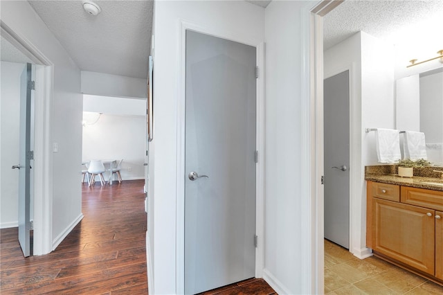 hallway featuring baseboards, a textured ceiling, and light wood finished floors