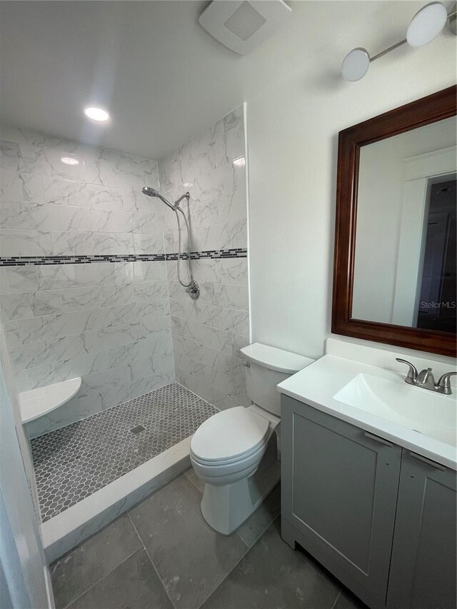 bathroom featuring tile patterned floors, toilet, a tile shower, and vanity