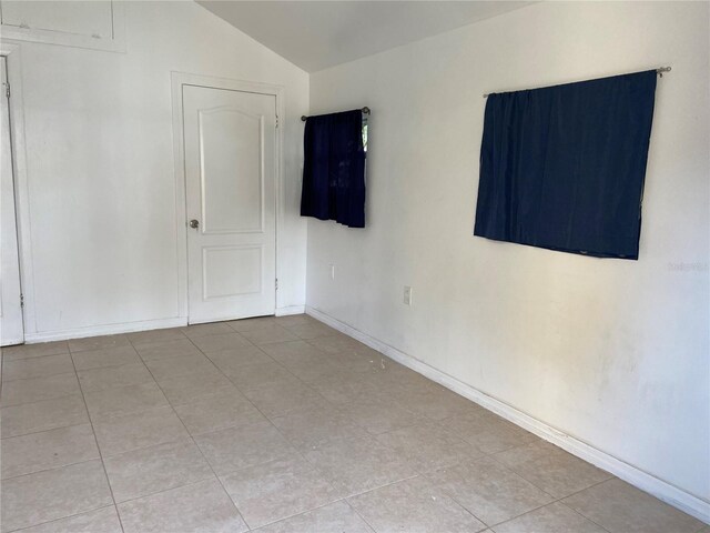 tiled empty room featuring vaulted ceiling