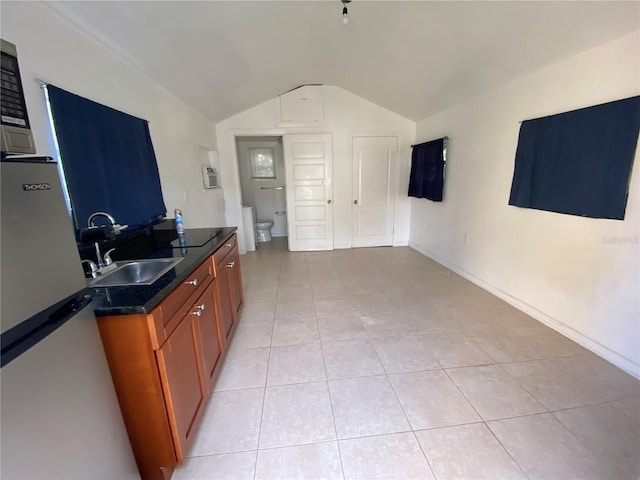 kitchen featuring lofted ceiling, stainless steel refrigerator, light tile patterned floors, and sink