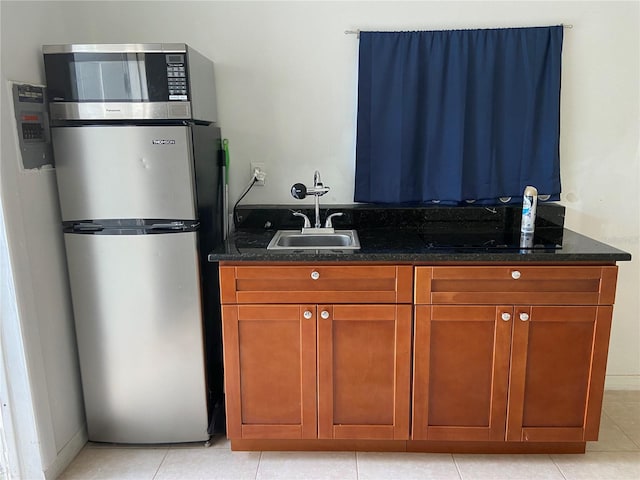 kitchen featuring stainless steel fridge, light tile patterned floors, sink, and dark stone counters