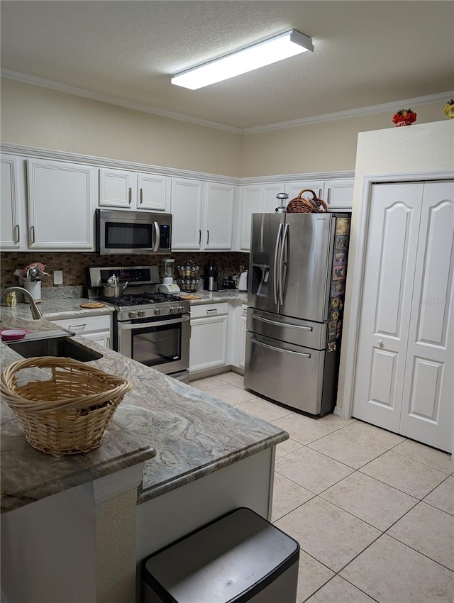 kitchen with decorative backsplash, appliances with stainless steel finishes, white cabinets, light tile patterned floors, and sink