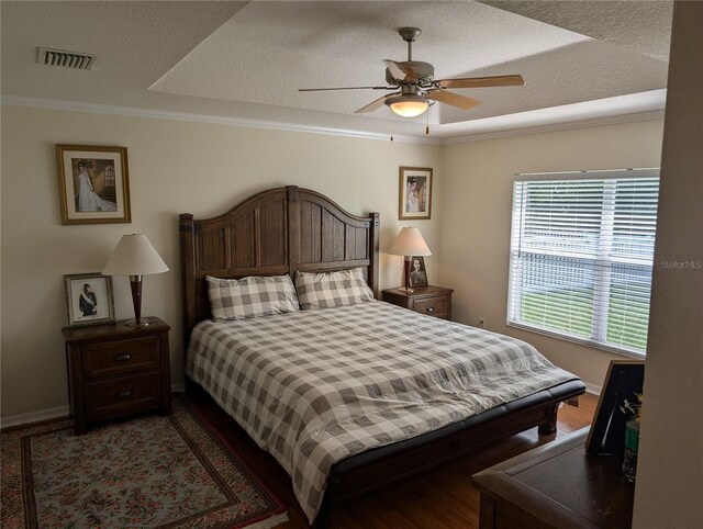 bedroom with ceiling fan, wood-type flooring, a textured ceiling, and a tray ceiling