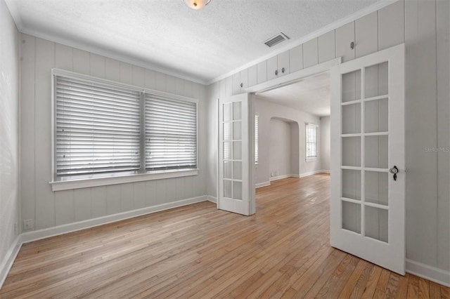 spare room with ornamental molding, light hardwood / wood-style floors, french doors, and a textured ceiling