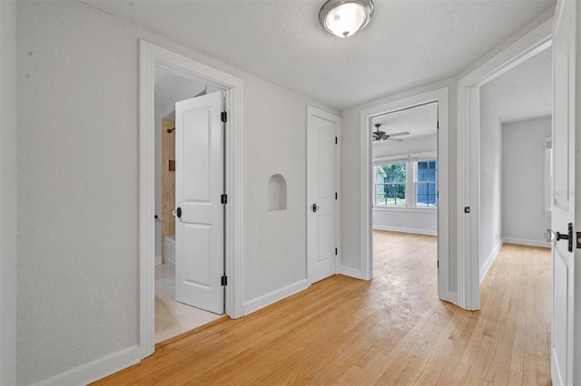 corridor with a textured ceiling and light wood-type flooring