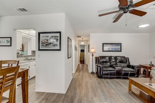 living room featuring light hardwood / wood-style flooring, a textured ceiling, and ceiling fan