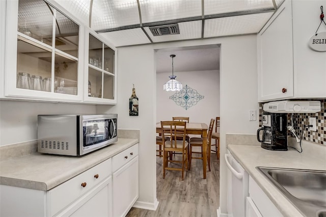 kitchen featuring white cabinetry, light countertops, stainless steel microwave, glass insert cabinets, and pendant lighting