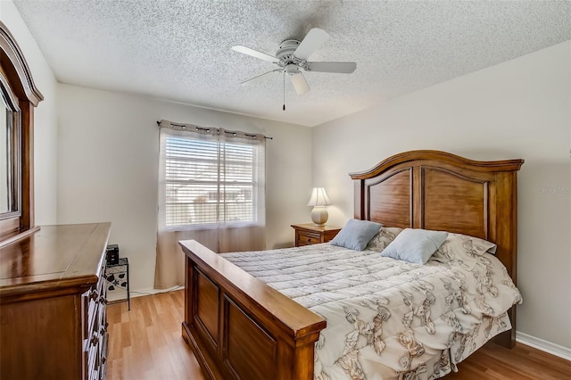 bedroom featuring a textured ceiling, baseboards, a ceiling fan, and light wood-style floors