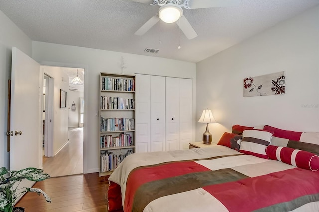 bedroom featuring dark wood-style flooring, a closet, visible vents, a ceiling fan, and a textured ceiling