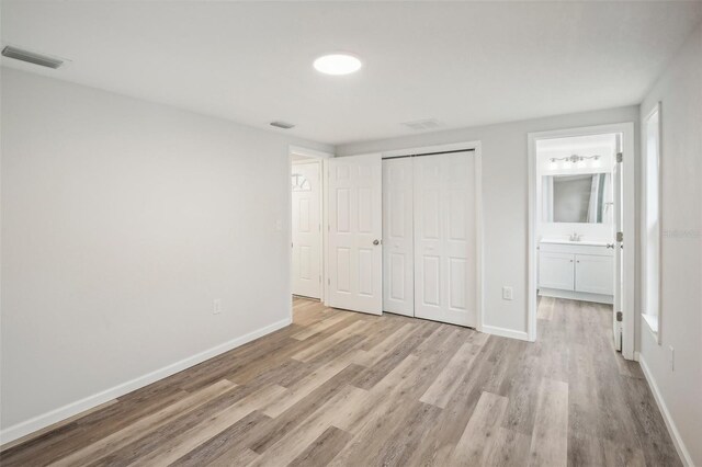 unfurnished bedroom with light hardwood / wood-style floors, sink, ensuite bath, and a closet