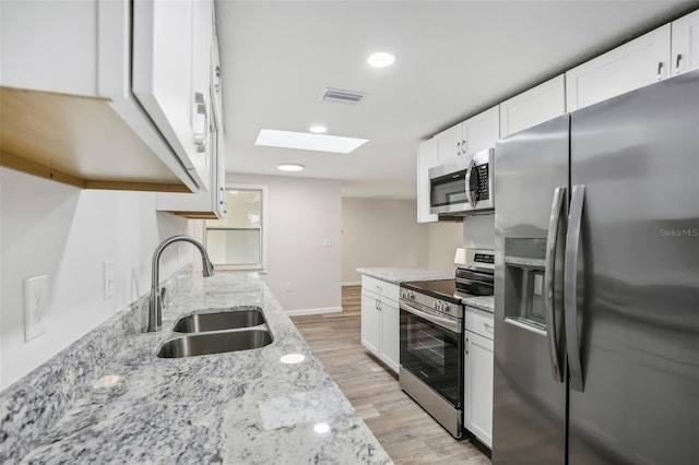 kitchen with a skylight, sink, light stone counters, appliances with stainless steel finishes, and light hardwood / wood-style flooring