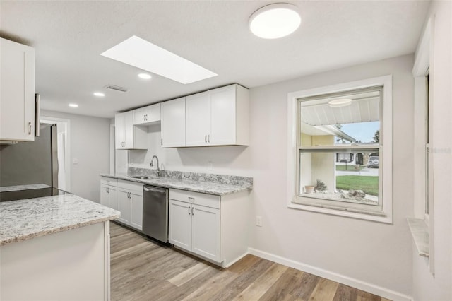 kitchen with a skylight, light hardwood / wood-style flooring, white cabinets, stainless steel appliances, and light stone countertops