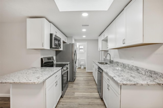 kitchen with a skylight, white cabinets, light hardwood / wood-style floors, appliances with stainless steel finishes, and sink