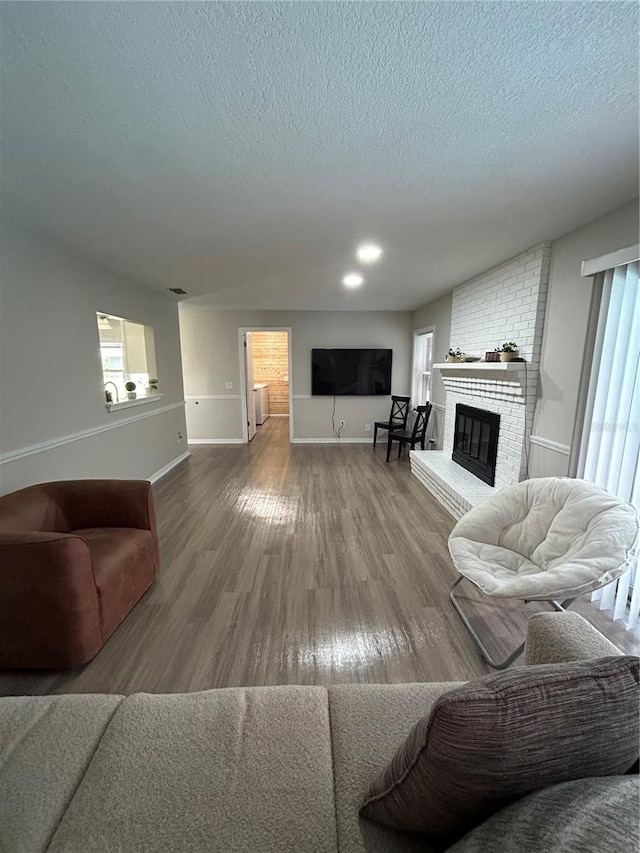 living room featuring a healthy amount of sunlight, wood-type flooring, a fireplace, and a textured ceiling