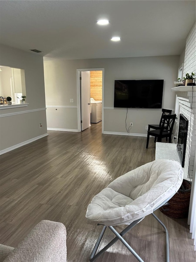 living room featuring a brick fireplace, washer and dryer, and dark hardwood / wood-style flooring