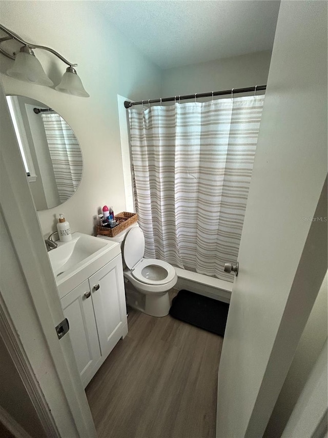 bathroom featuring wood-type flooring, a textured ceiling, walk in shower, vanity, and toilet