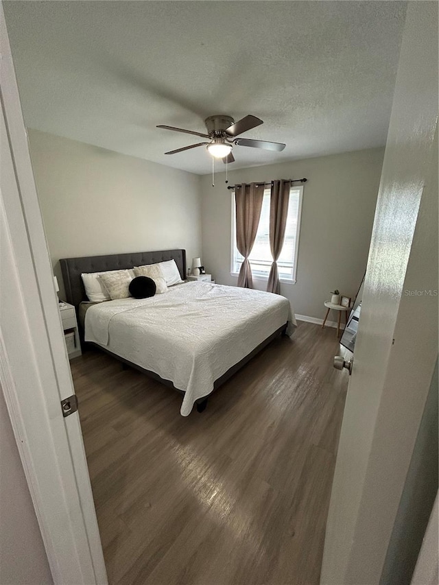 bedroom with ceiling fan, a textured ceiling, and dark hardwood / wood-style flooring