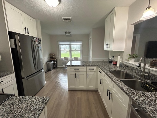 kitchen with kitchen peninsula, dark stone counters, white cabinetry, stainless steel refrigerator, and light wood-type flooring