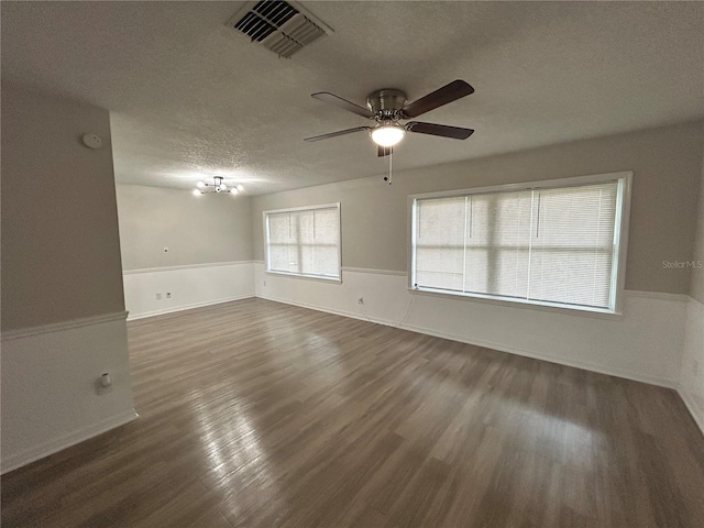 empty room featuring ceiling fan with notable chandelier, a textured ceiling, and dark hardwood / wood-style flooring