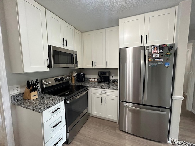 kitchen featuring dark stone counters, light hardwood / wood-style floors, a textured ceiling, white cabinets, and appliances with stainless steel finishes