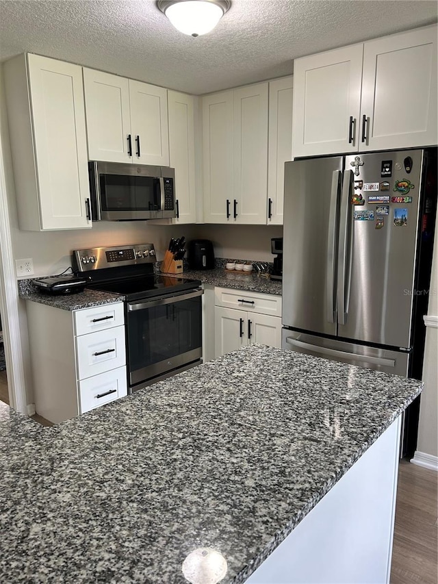 kitchen with stainless steel appliances, white cabinets, a textured ceiling, and hardwood / wood-style floors