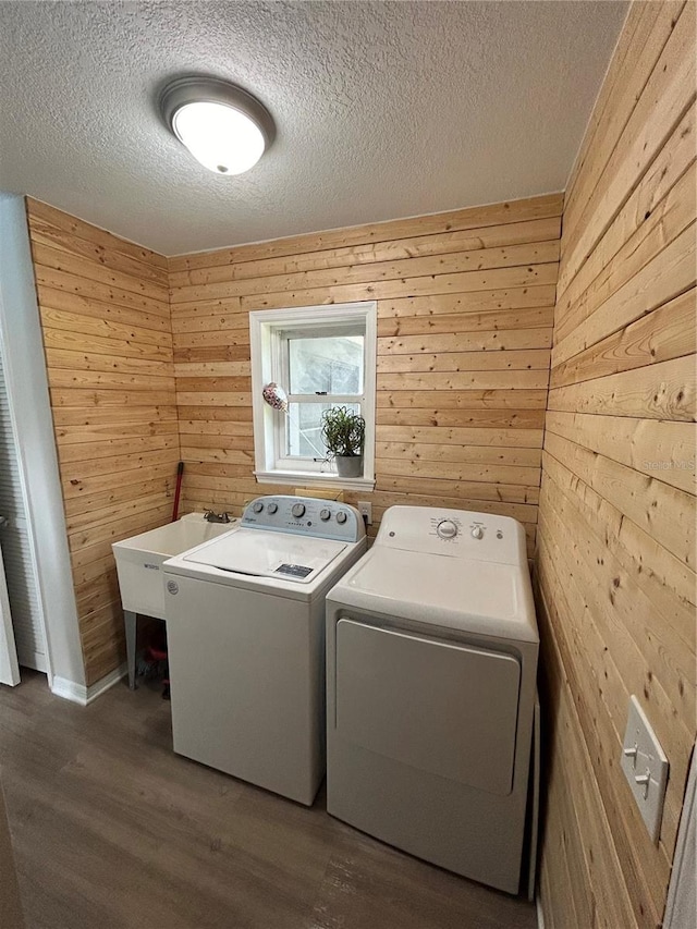 laundry area with sink, wood-type flooring, a textured ceiling, wooden walls, and washer and dryer