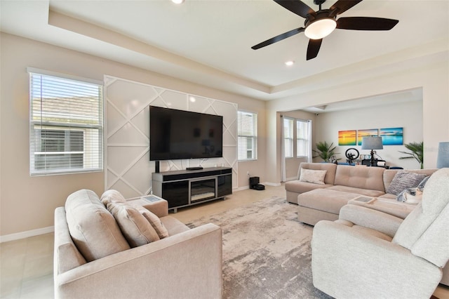 living room featuring a healthy amount of sunlight, a raised ceiling, and ceiling fan