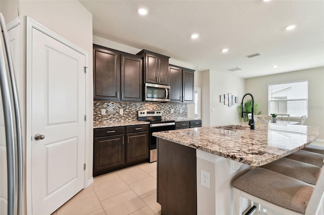 kitchen featuring appliances with stainless steel finishes, a kitchen bar, tasteful backsplash, and a kitchen island with sink