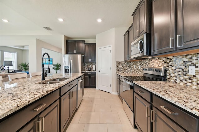 kitchen with appliances with stainless steel finishes, light tile patterned floors, tasteful backsplash, and light stone counters