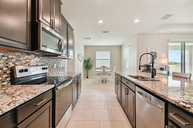 kitchen with appliances with stainless steel finishes, light tile patterned floors, a wealth of natural light, and tasteful backsplash