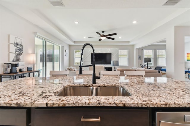 kitchen with a tray ceiling, light stone counters, sink, and ceiling fan