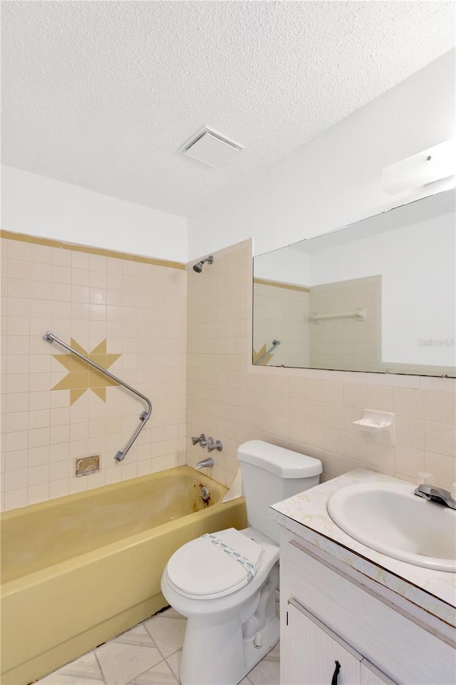 full bathroom with tile patterned flooring, toilet, tiled shower / bath combo, vanity, and tile walls