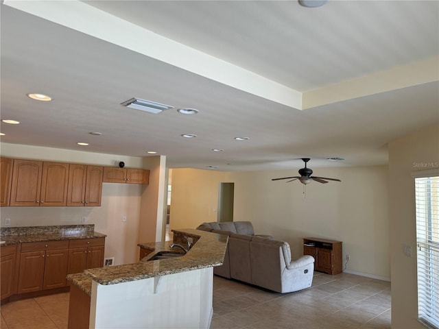 kitchen featuring dark stone counters, sink, light tile patterned floors, and ceiling fan