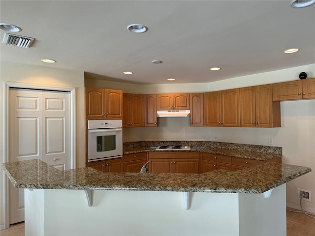 kitchen featuring a breakfast bar, dark stone counters, light tile patterned flooring, and white appliances