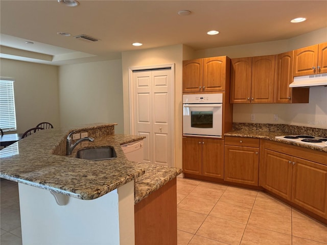 kitchen featuring sink, light tile patterned flooring, a kitchen island with sink, and white appliances