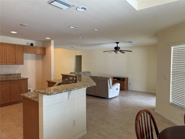 kitchen with light tile patterned floors, ceiling fan, a kitchen breakfast bar, stone counters, and sink