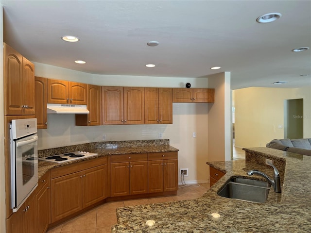 kitchen featuring dark stone counters, light tile patterned floors, white appliances, and sink