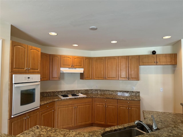 kitchen with sink, light tile patterned flooring, dark stone counters, and white appliances