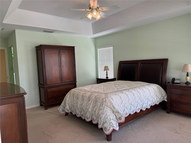 bedroom featuring ceiling fan, light carpet, and a tray ceiling